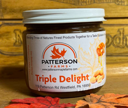 Patterson Farms Triple Delight Jar of Patterson Farms Triple Delight, featuring a blend of maple syrup, peanuts, and honey, set against autumn leaves and a wooden background. The label includes the address and website for Patterson Farms in Westfield, PA.
