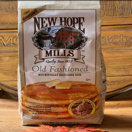5231f73f-e100-4344-ad2a-cd750bddce50 Package of New Hope Mills Old Fashioned Buckwheat Pancake Mix, featuring a stack of pancakes drizzled with syrup, set against a rustic wooden background. The bag highlights its gourmet quality and includes the brand's logo and product information.