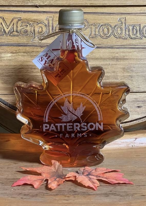 Terri Patterson - IMG_6457 Maple syrup in a decorative leaf-shaped bottle from Patterson Farms, displayed on a wooden surface with artificial autumn leaves.